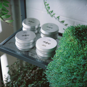 dollop pomade stacked on shelf surrounded by green pot plants